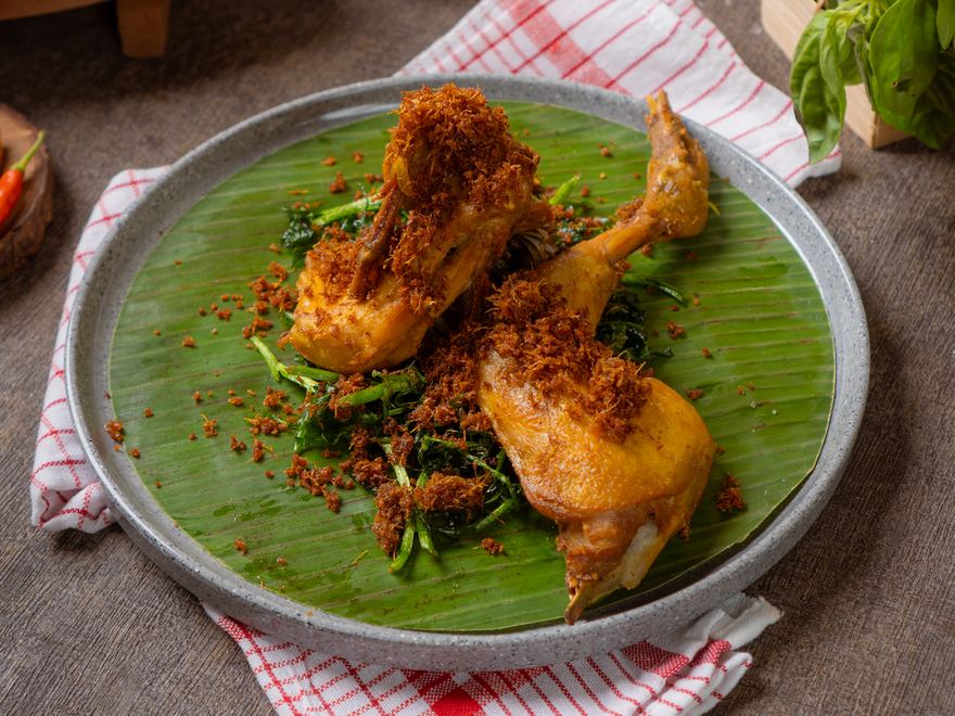 Ayam Goreng Laja — ayam goreng berbumbu kuning bertabur serundeng laja, disajikan di atas daun pisang dengan kemangi goreng