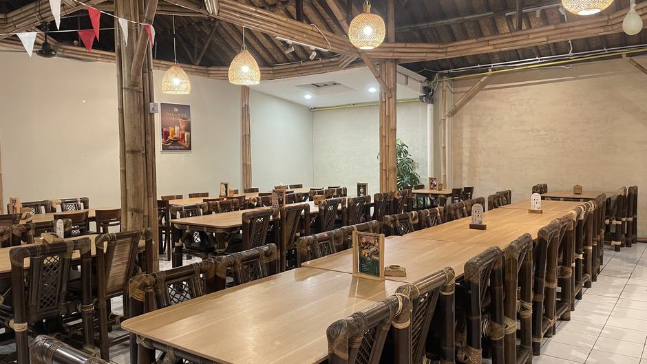 Ruang makan RM Awi Legit — meja panjang dan kursi bambu di bawah atap saung dengan lampu anyaman rotan
