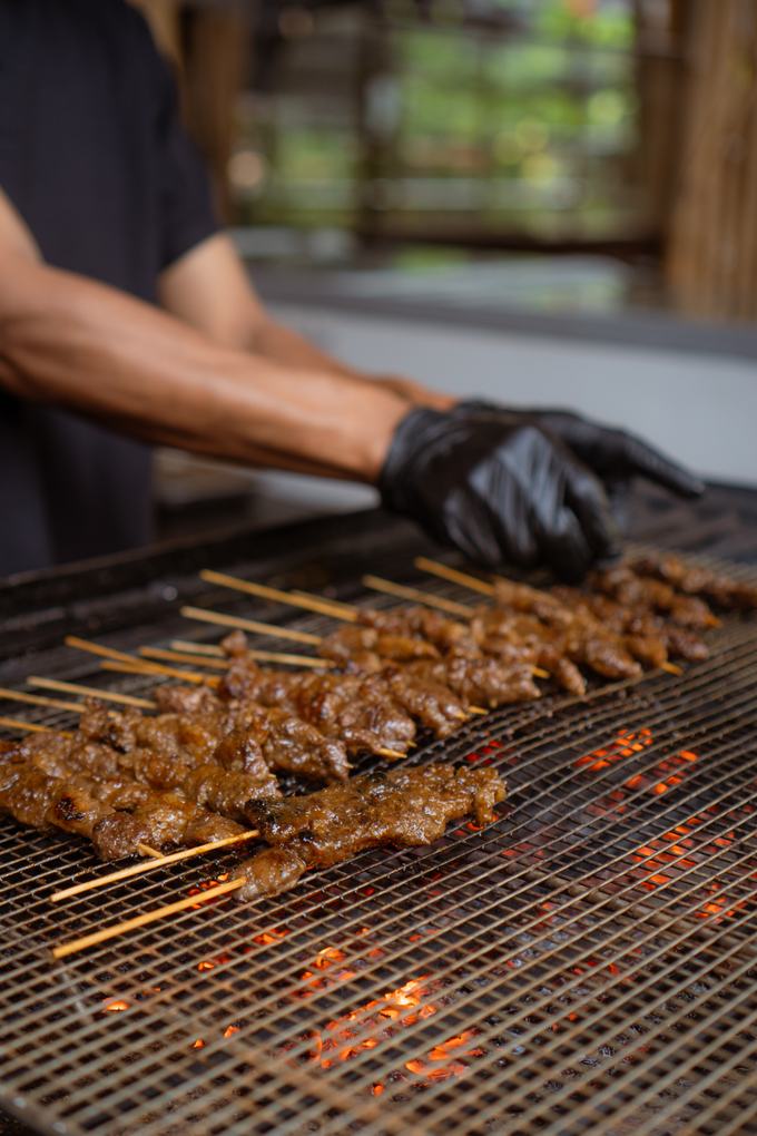 Juru masak membakar puluhan tusuk sate di atas bara arang di area terbuka RM Awi Legit