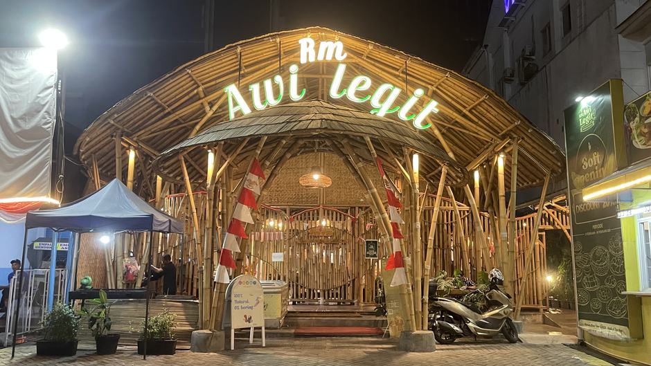 Tampak depan RM Awi Legit di malam hari — bangunan saung bambu dengan papan nama menyala di Jl. Surapati, Bandung
